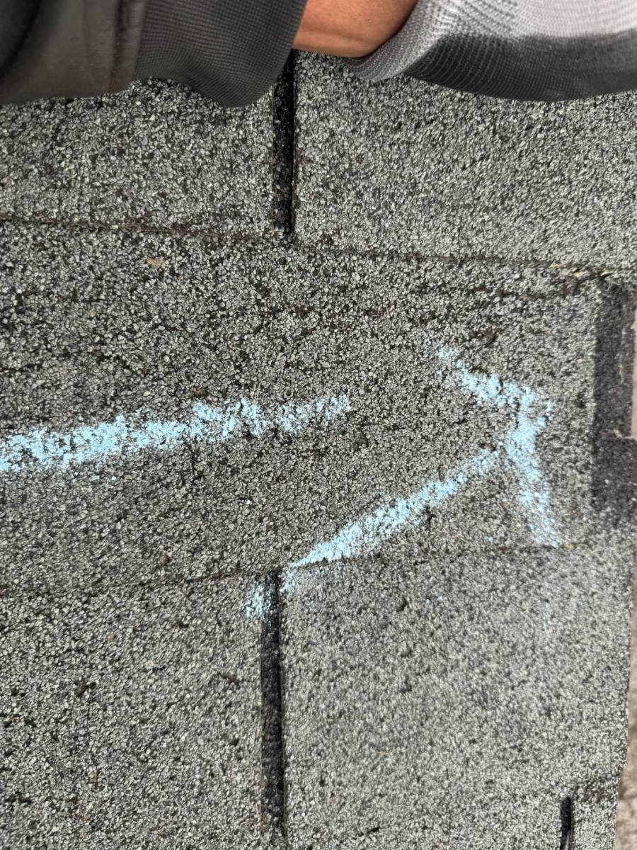 Chalk marking crease lines running across asphalt shingle courses